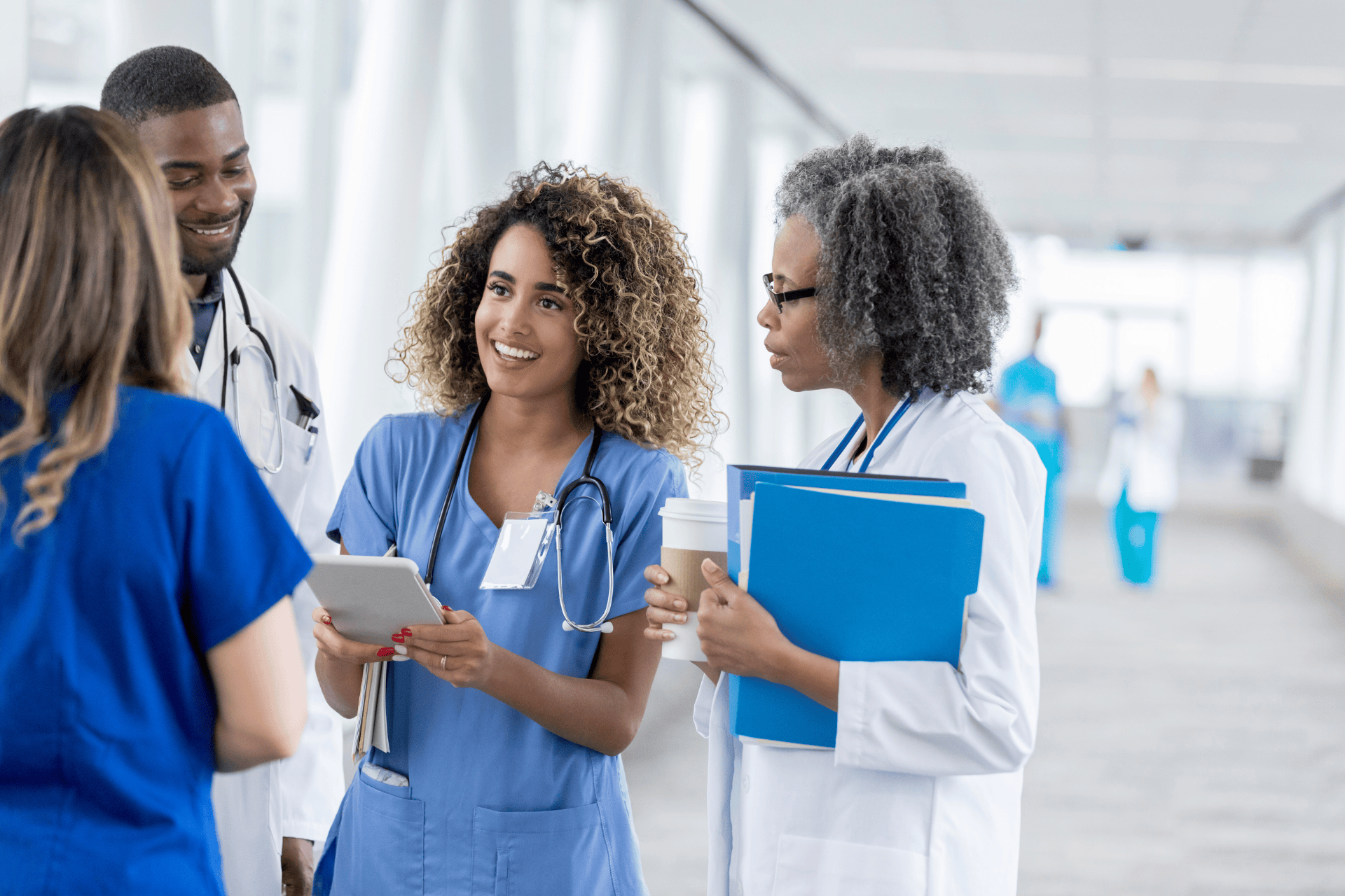Group of healthcare professionals talking and smiling in a hospital hallway.