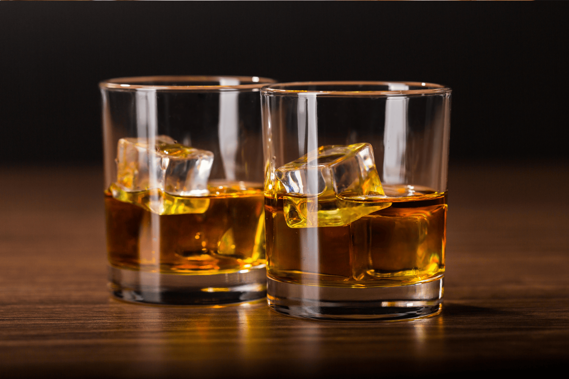 Two glasses of whiskey with ice cubes on a wooden table.