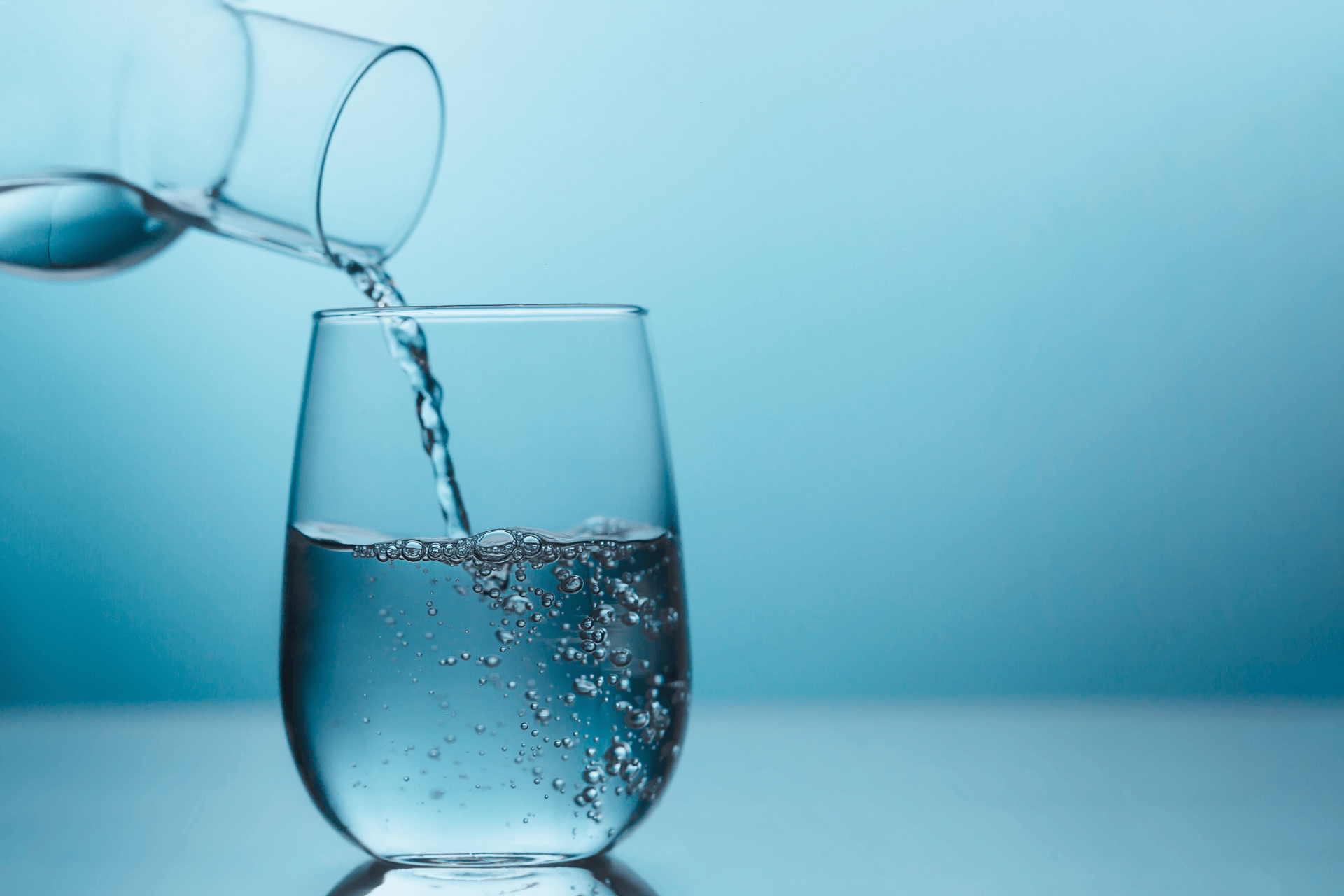 Water being poured from a glass bottle into a clear glass.