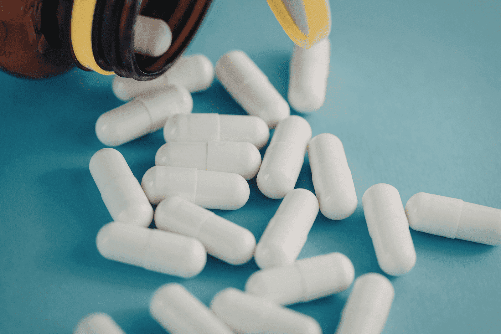 White capsules spilled from a pill bottle onto a blue surface.