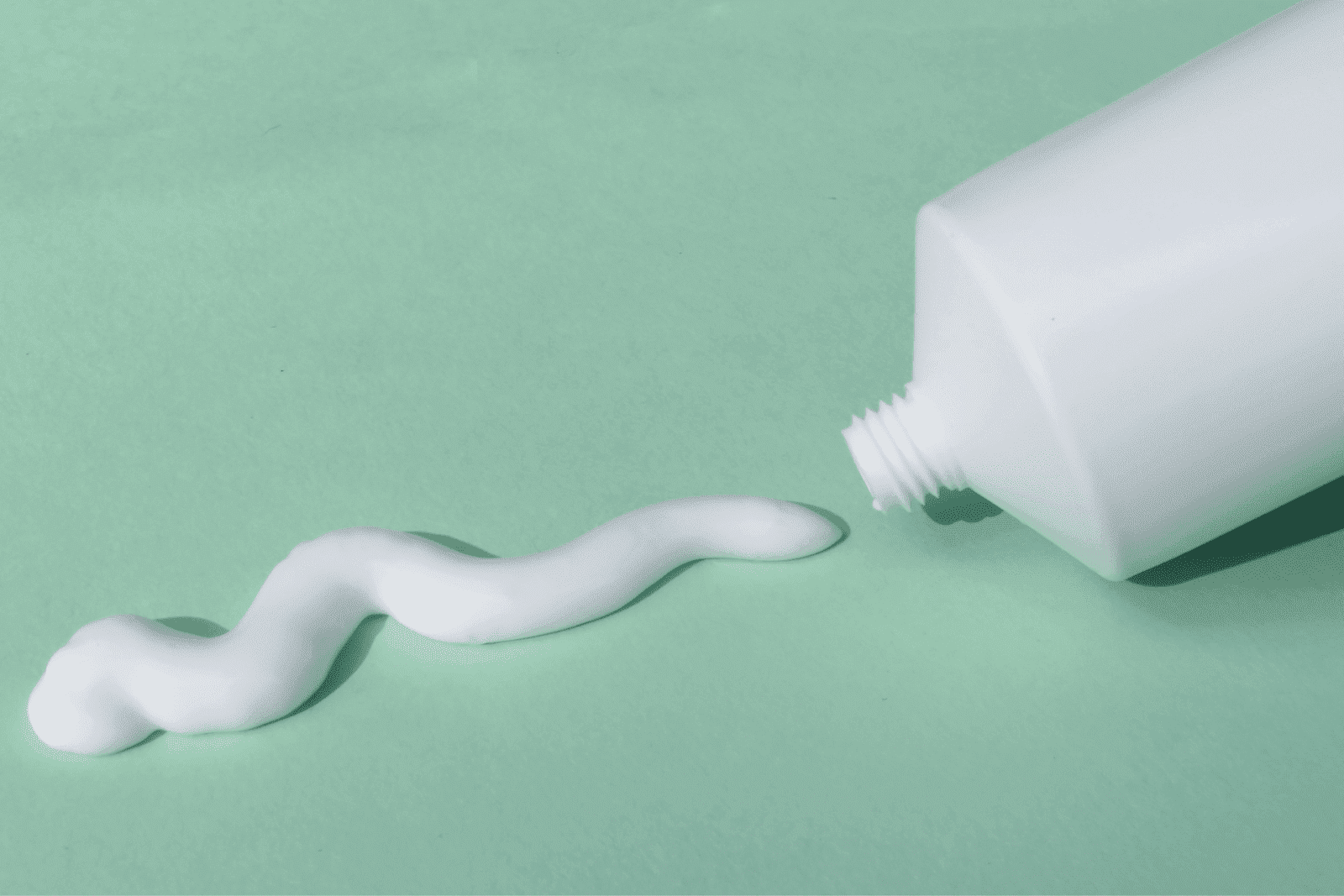 White cream squeezed from a tube onto a mint-green surface.