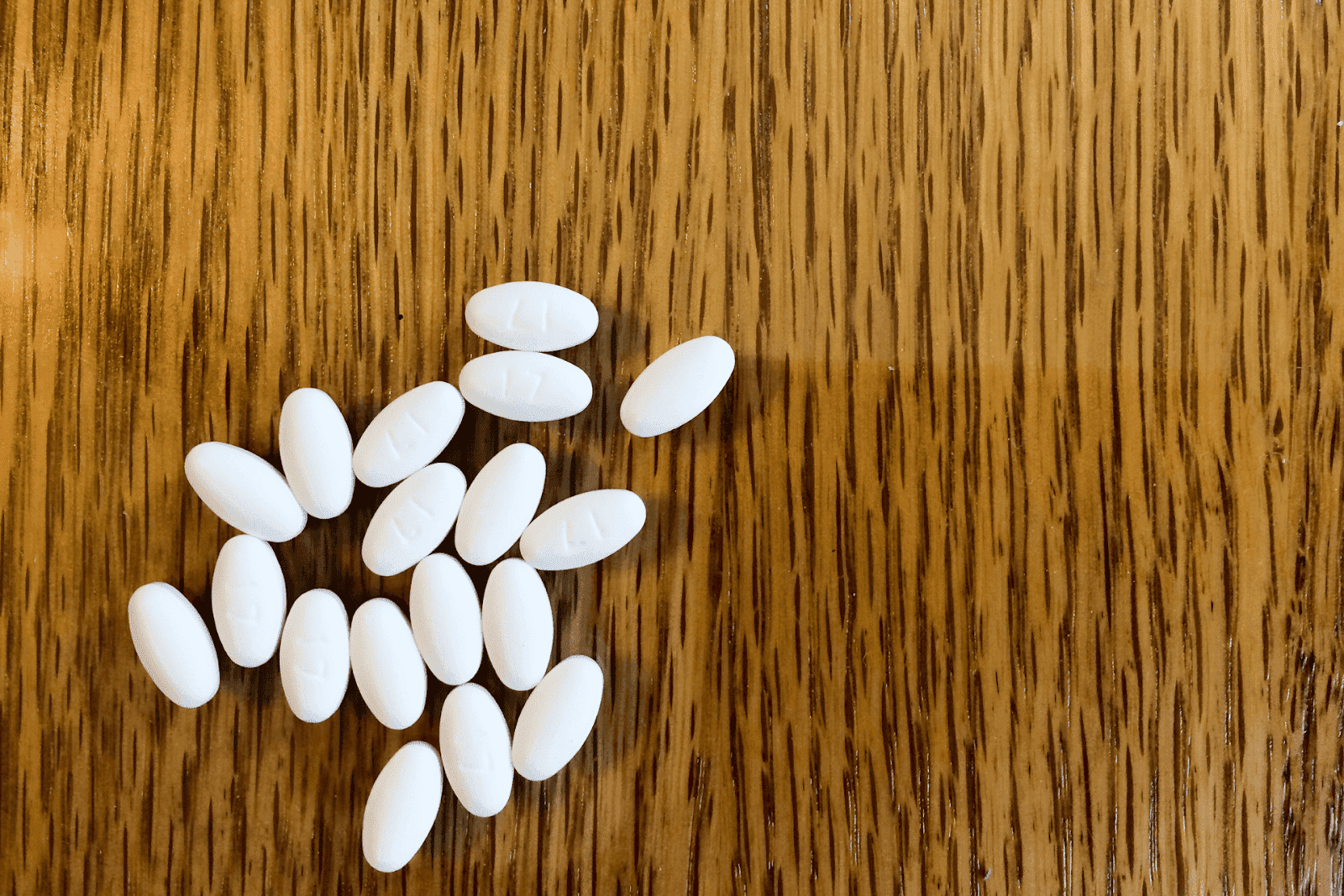 White oval pills scattered on a wooden surface.