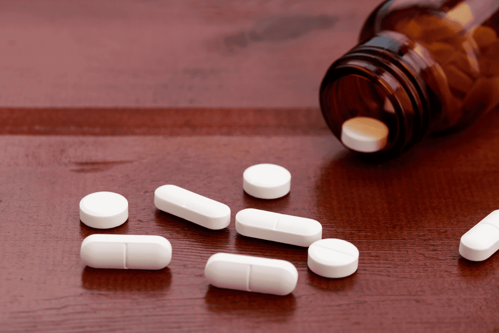 White pills spilled from a brown bottle onto a wooden table.