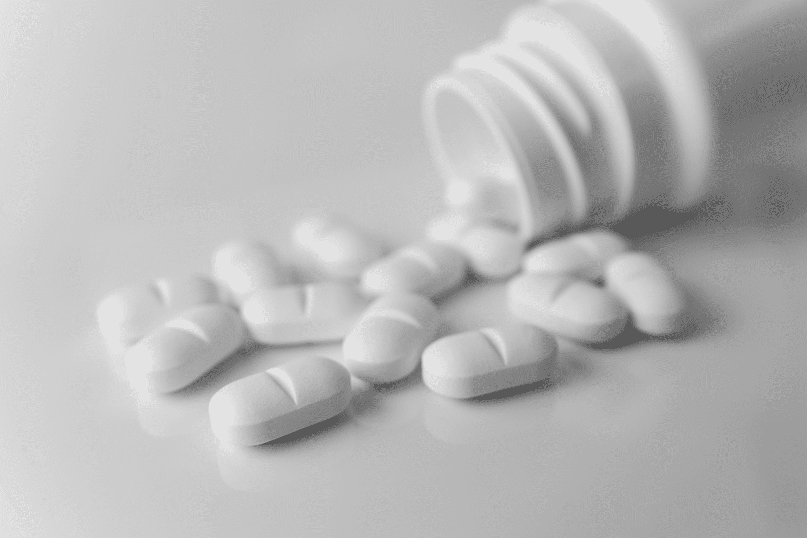 White tablets spilled from an open pill bottle onto a smooth surface.