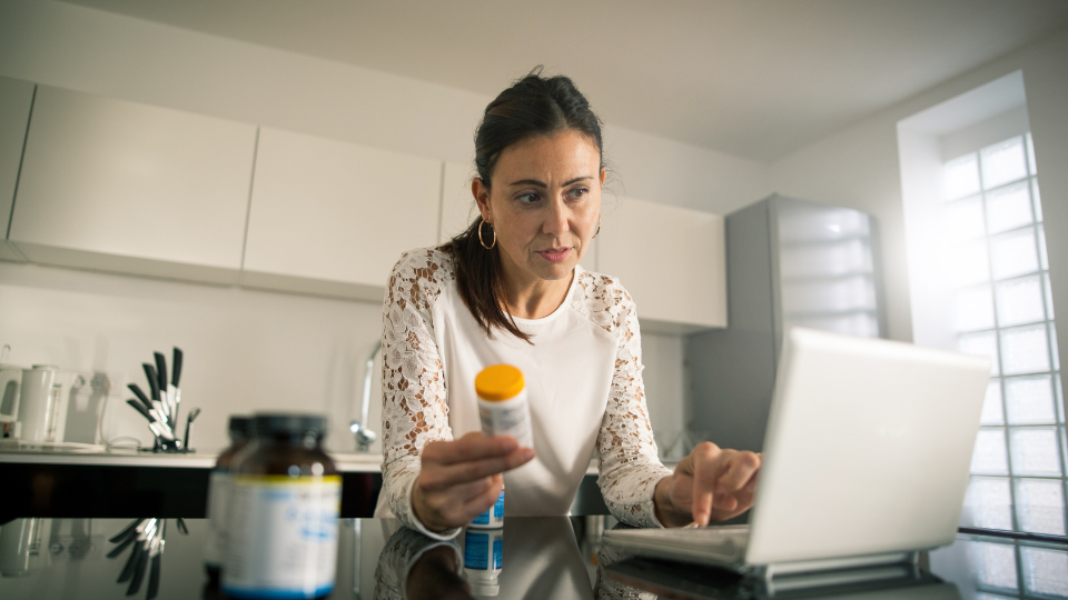 A woman holding a prescription bottle while using a laptop.