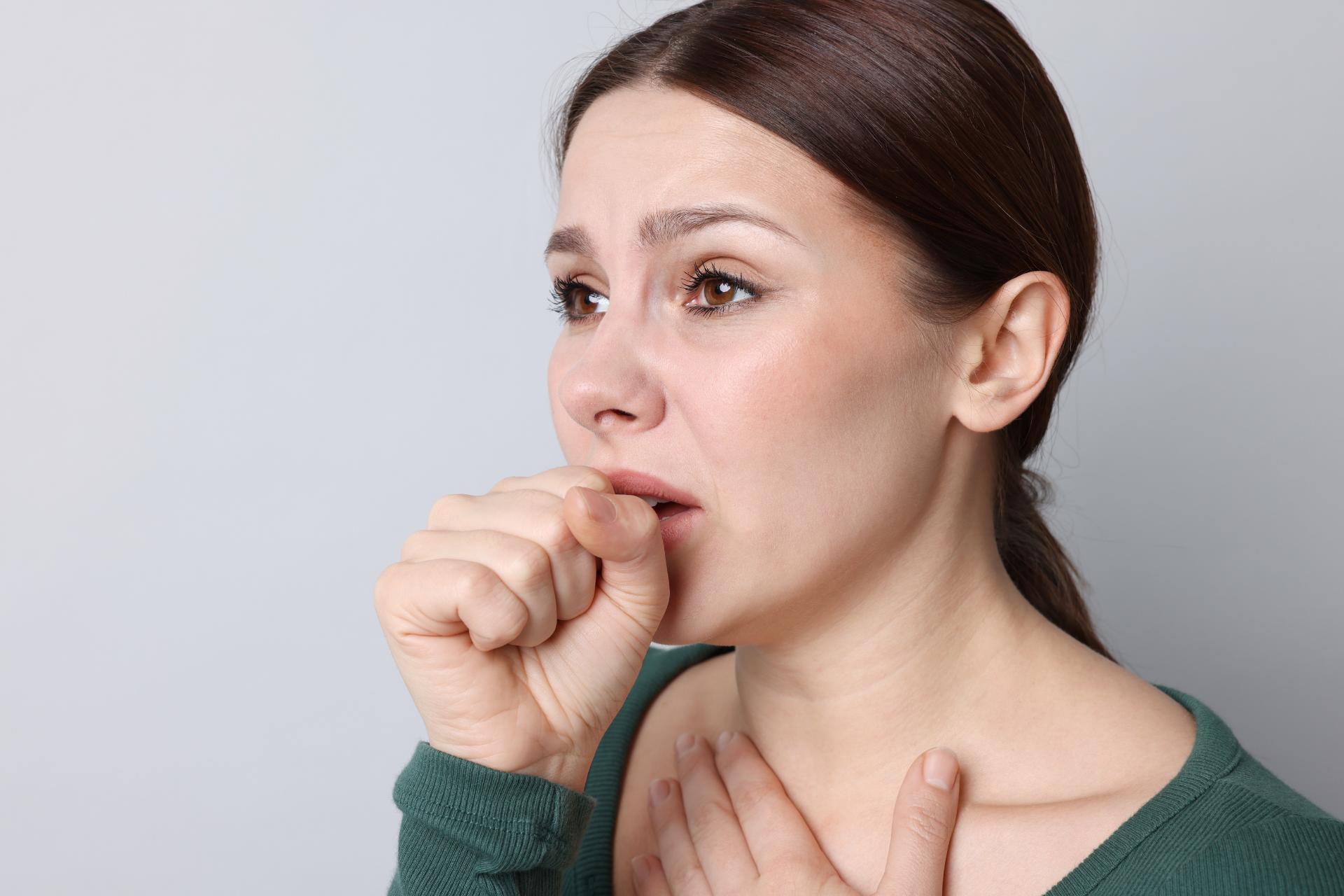 Woman coughing into her fist while holding her chest, appearing concerned or unwell