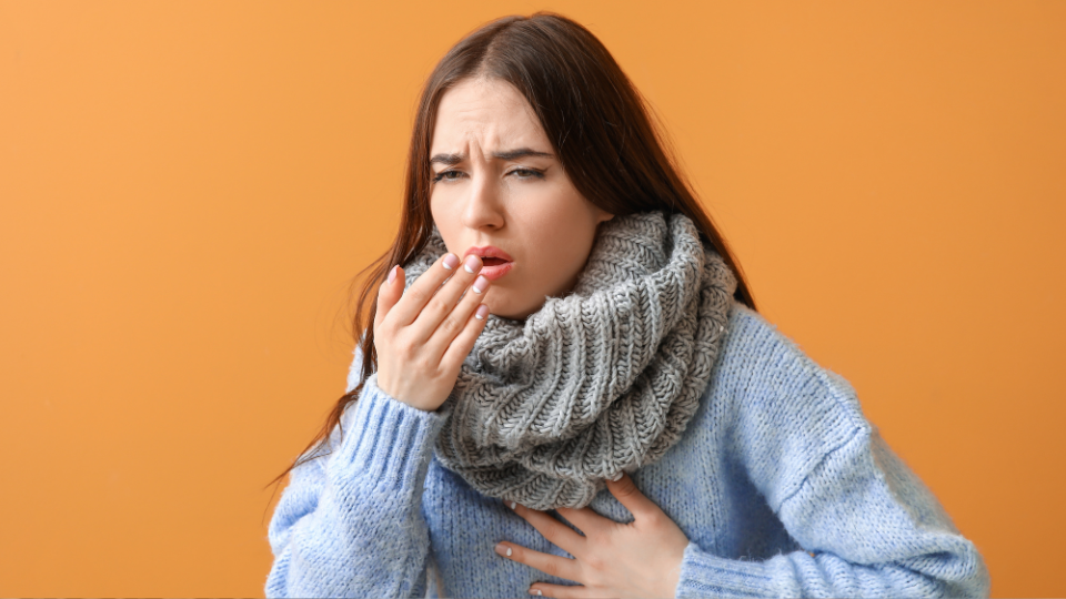 Woman coughing into hand and holding chest with other hand.