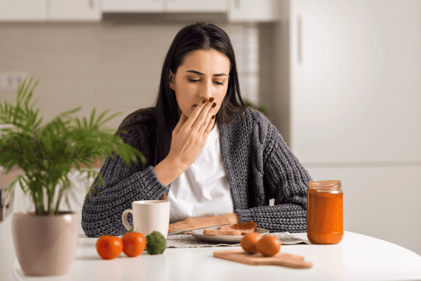 Woman covering mouth with nausea while sitting at a table.