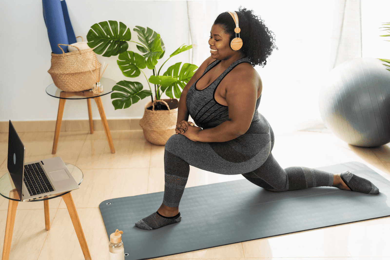 Woman doing a lunge stretch on a yoga mat at home while following a workout on a laptop