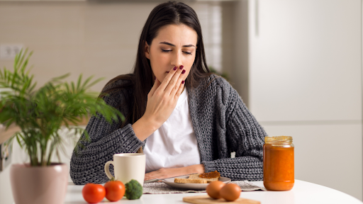 Woman covering her mouth and sitting at table with food in front of her.