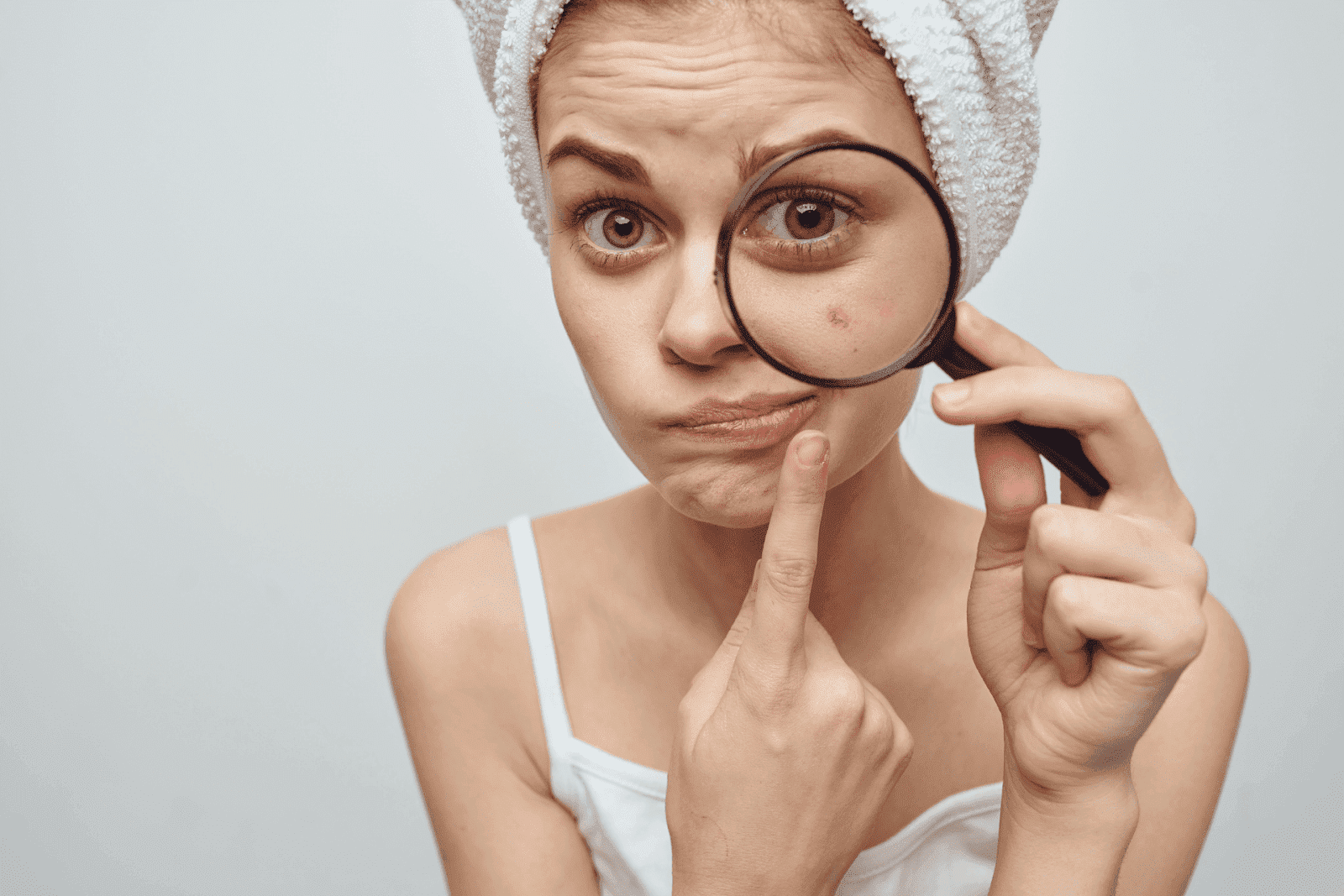 Woman examining a pimple with a magnifying glass.