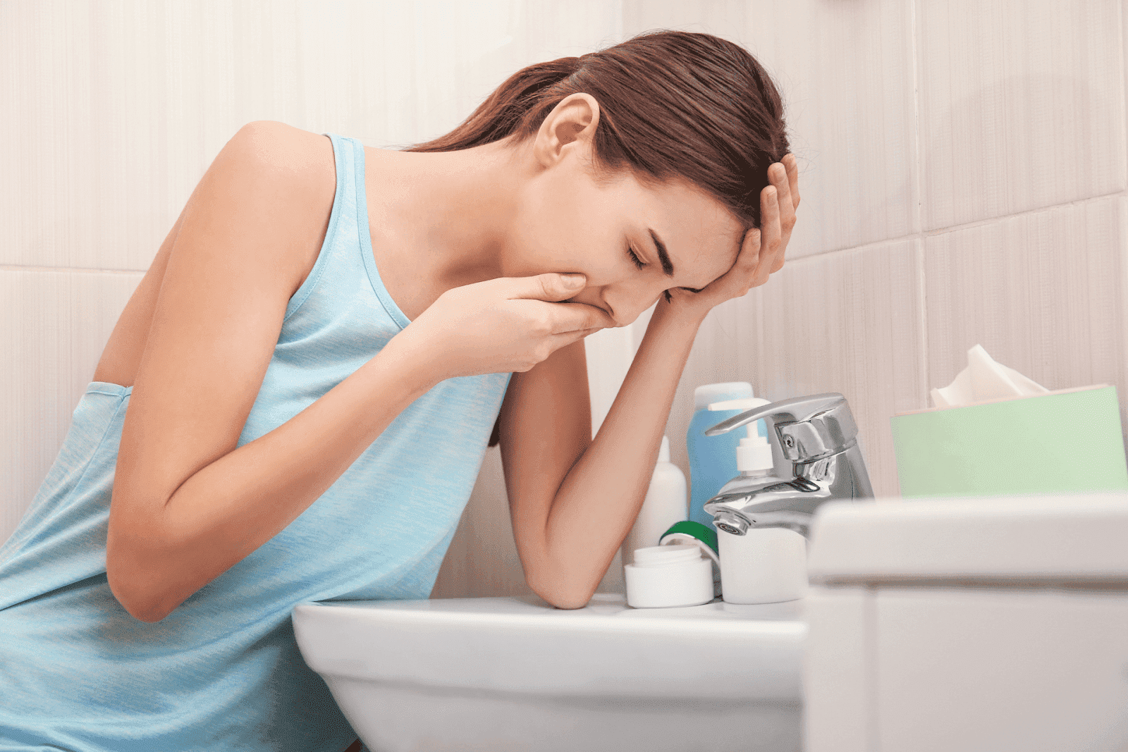 Woman feeling nauseous and leaning over the bathroom sink.