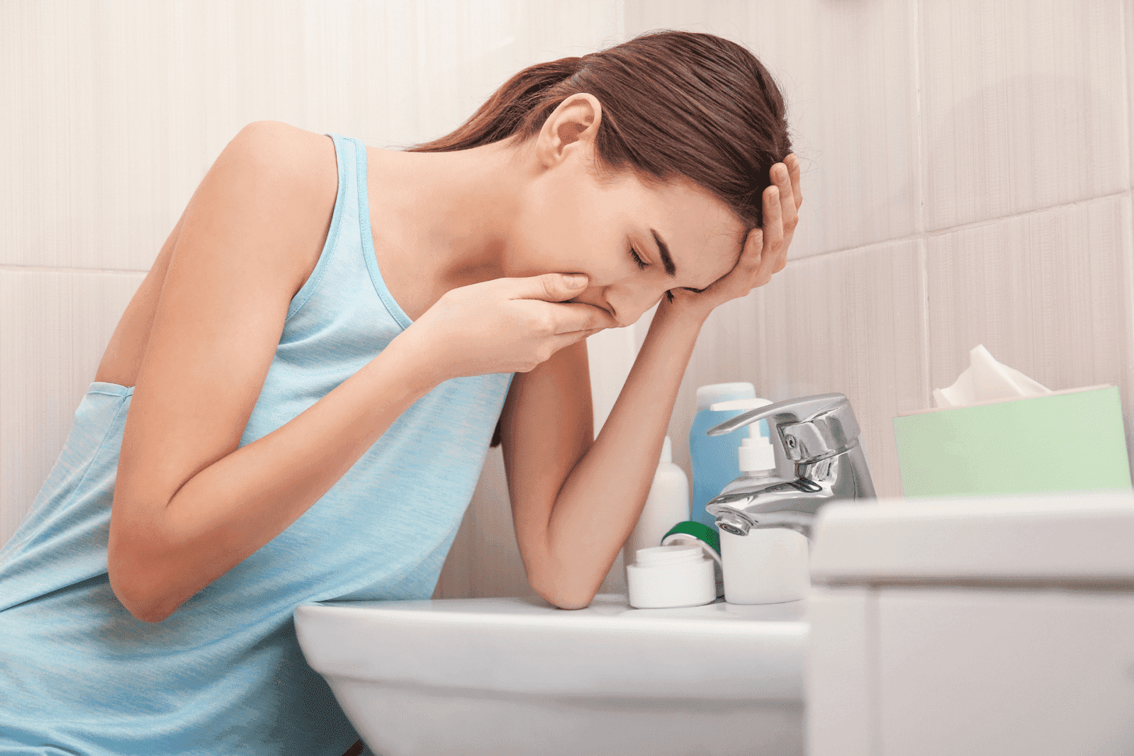 Woman feeling sick and vomiting into a bathroom sink.
