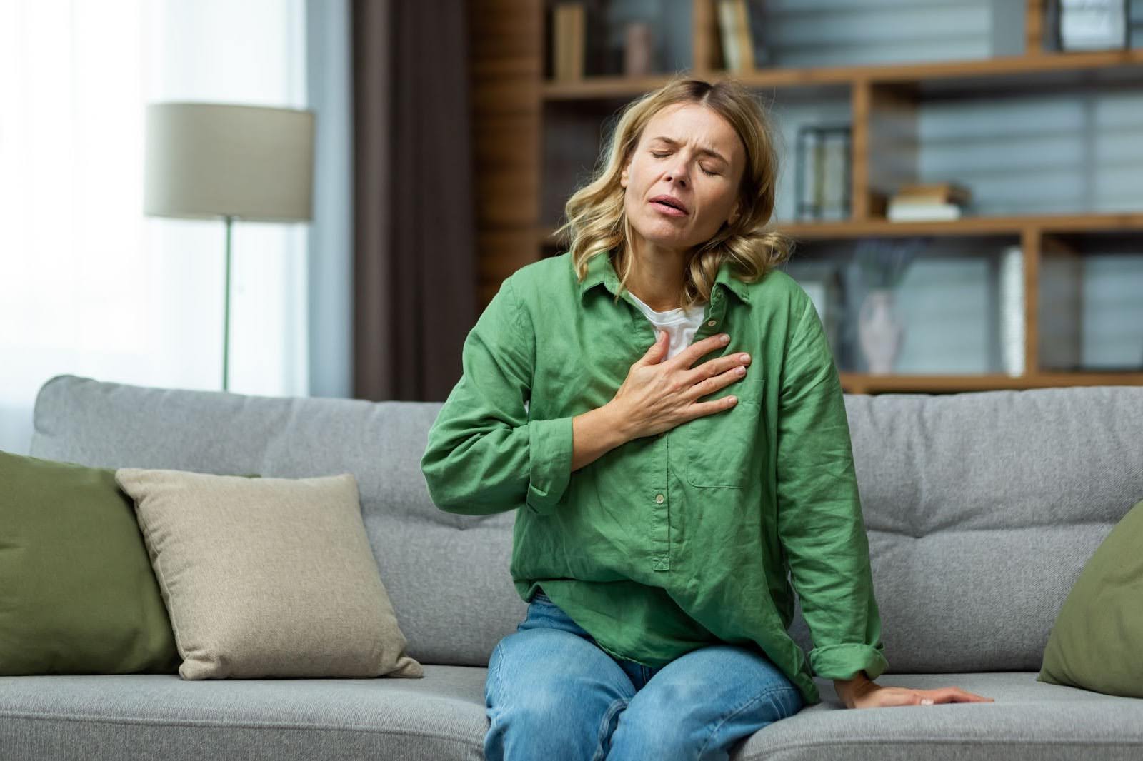Woman holding her chest in pain, sitting on the sofa