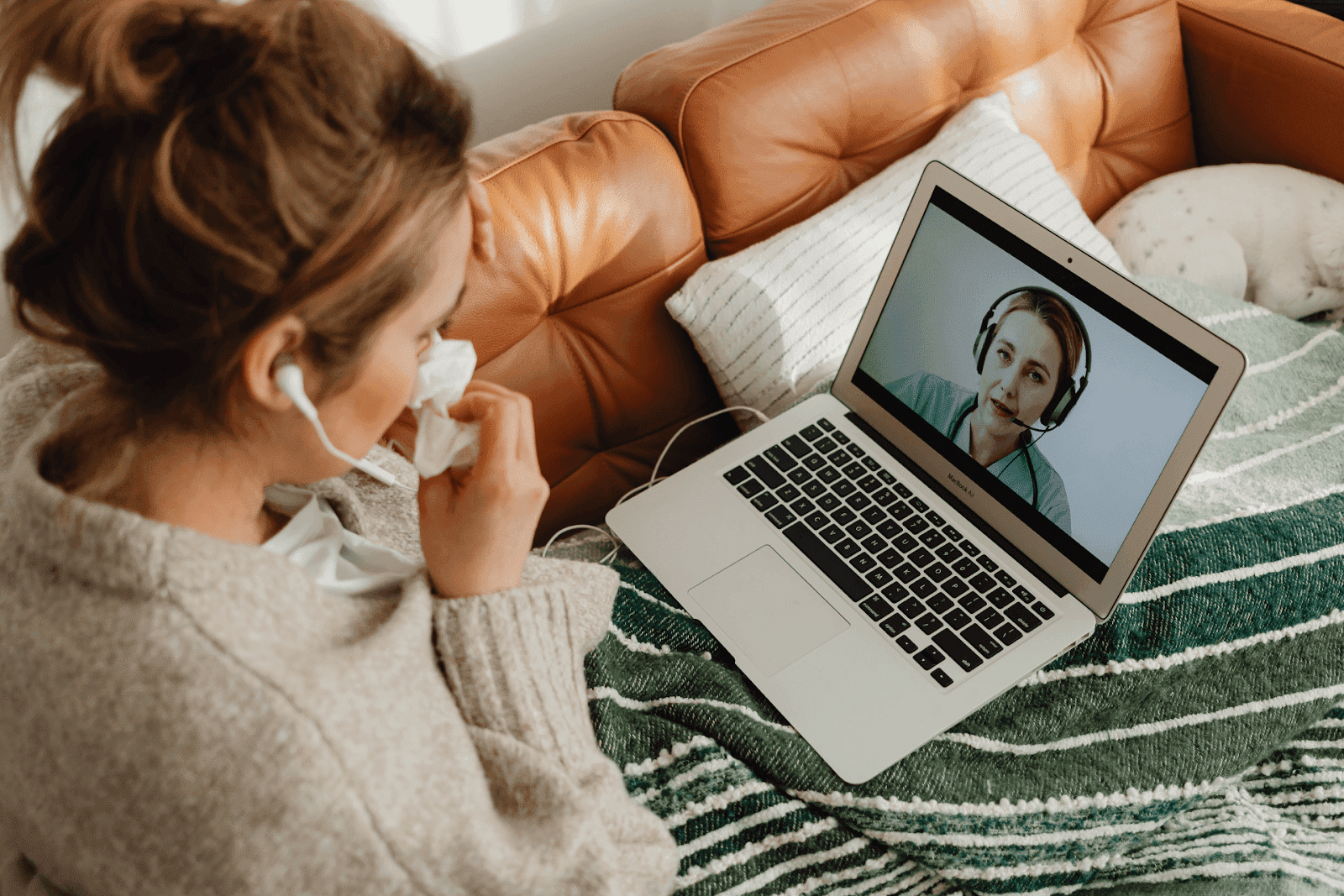 Woman having an online medical consultation while sick, holding a tissue