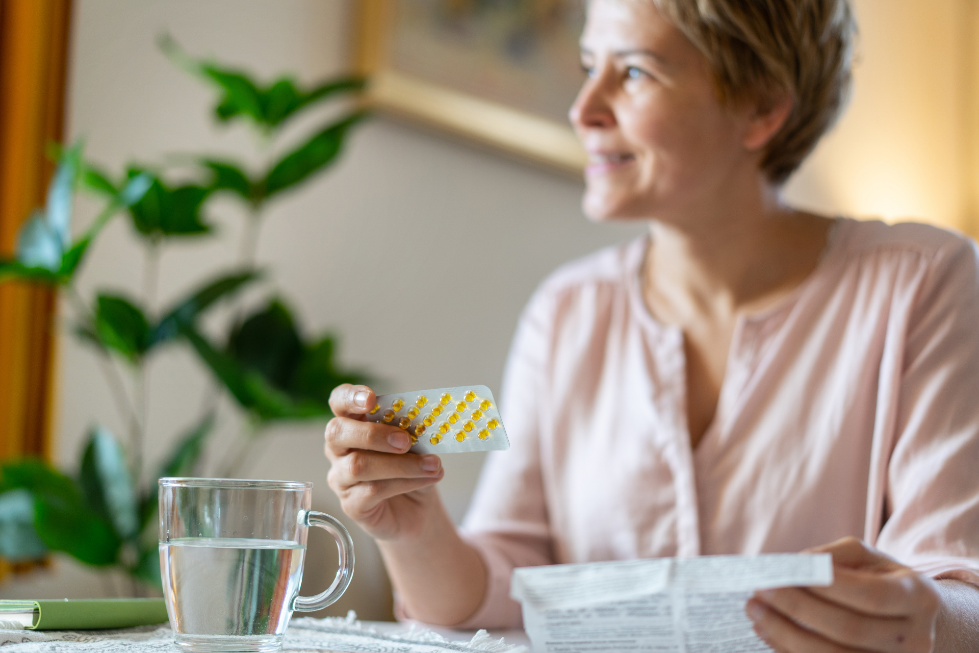 Woman holding a blister pack of pills and medication instructions beside a glass of water