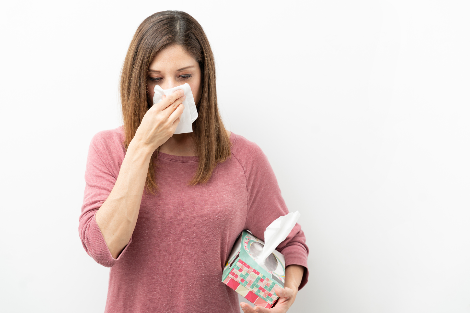 Woman holding a tissue to her nose while holding a tissue box, appearing to have a cold or nasal congestion