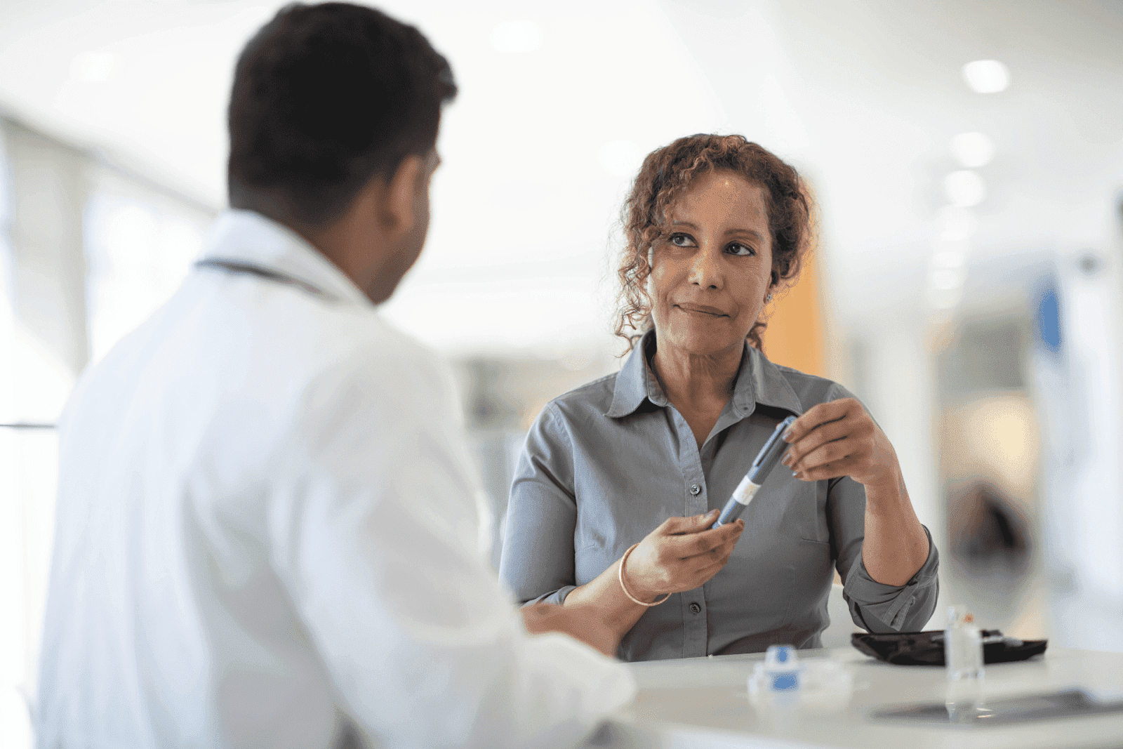 Woman holding an insulin pen and discussing with her doctor in a clinical setting