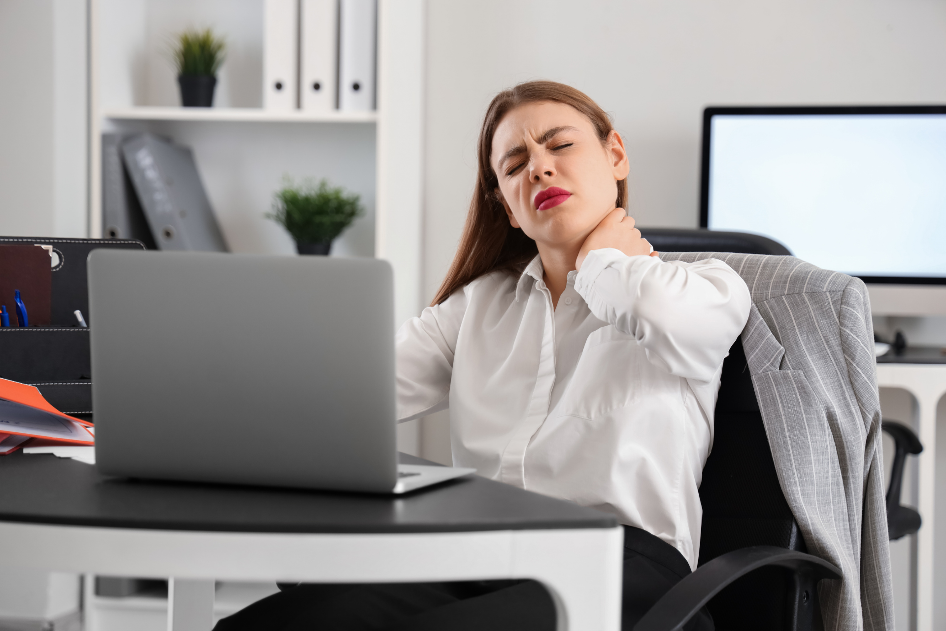 Woman holding her neck in pain while working at a laptop in an office