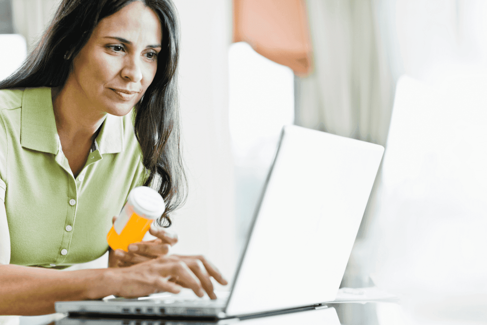 Woman holding prescription bottle while using laptop.