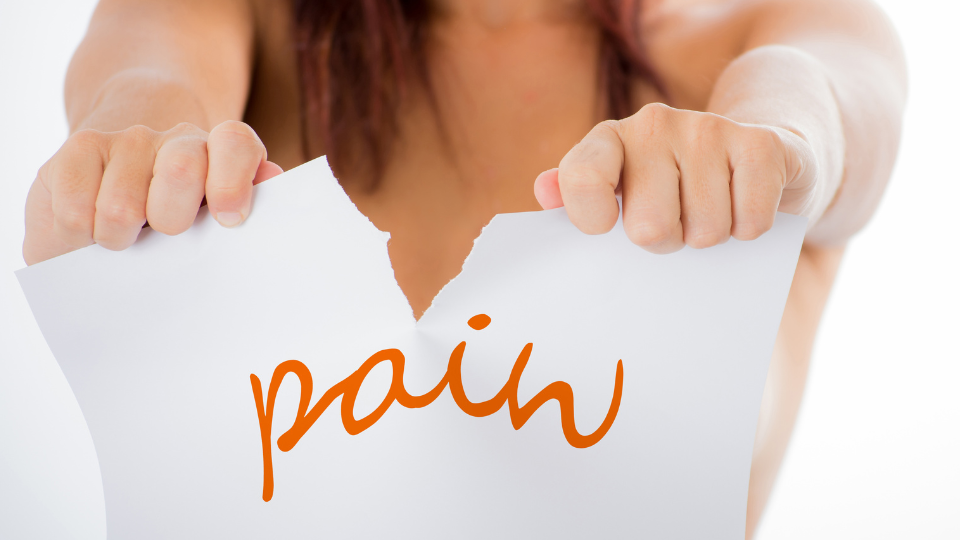 Woman holding and tearing up a paper sign saying "pain".