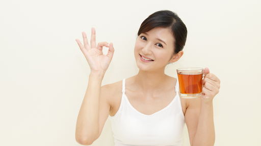 Woman showing "ok" sign with one hand and holding a tea with the other hand.