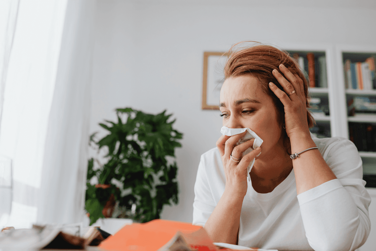 Woman in a white shirt holding a tissue to her nose, looking distressed.