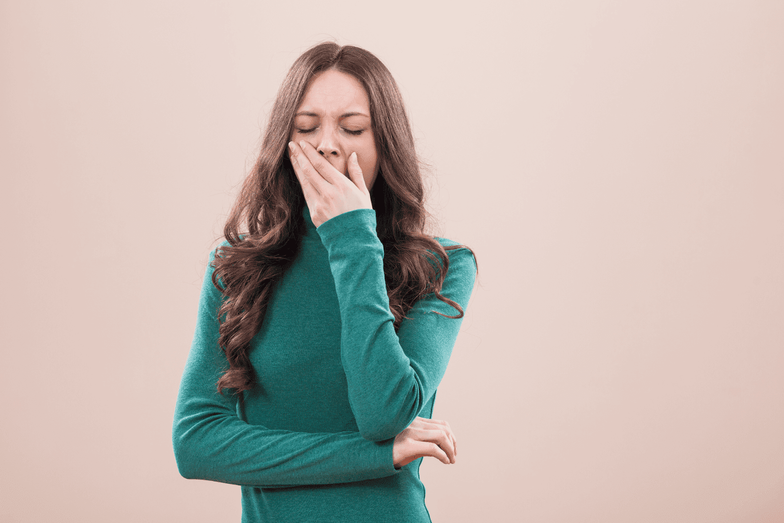 Woman in green sweater yawning with hand covering mouth.
