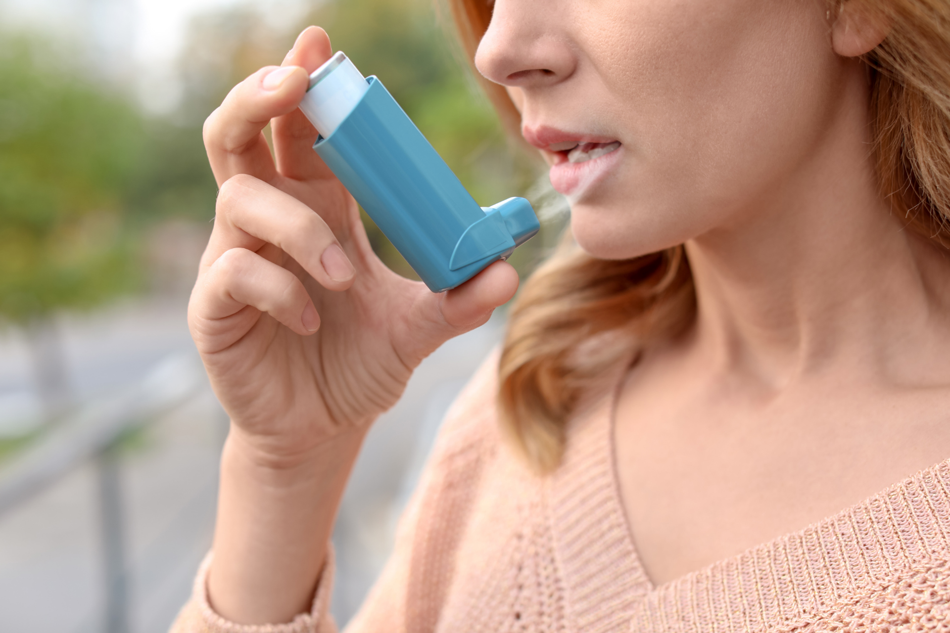 Woman using a blue asthma inhaler outdoors