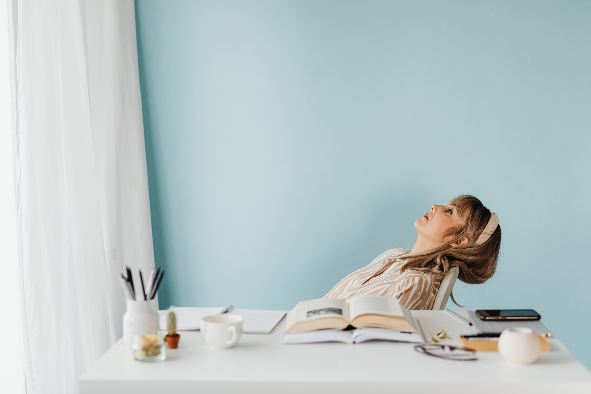 Woman leaning back in a chair at a desk, looking upward and appearing tired or stressed in a home workspace