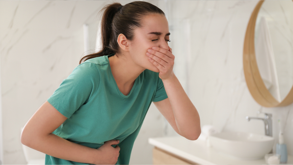 Woman in bathroom covering mouth with one hand and holding stomach with the other appearing to want to vomit