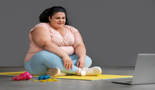 A woman on a workout mat exercising with a laptop open on the floor