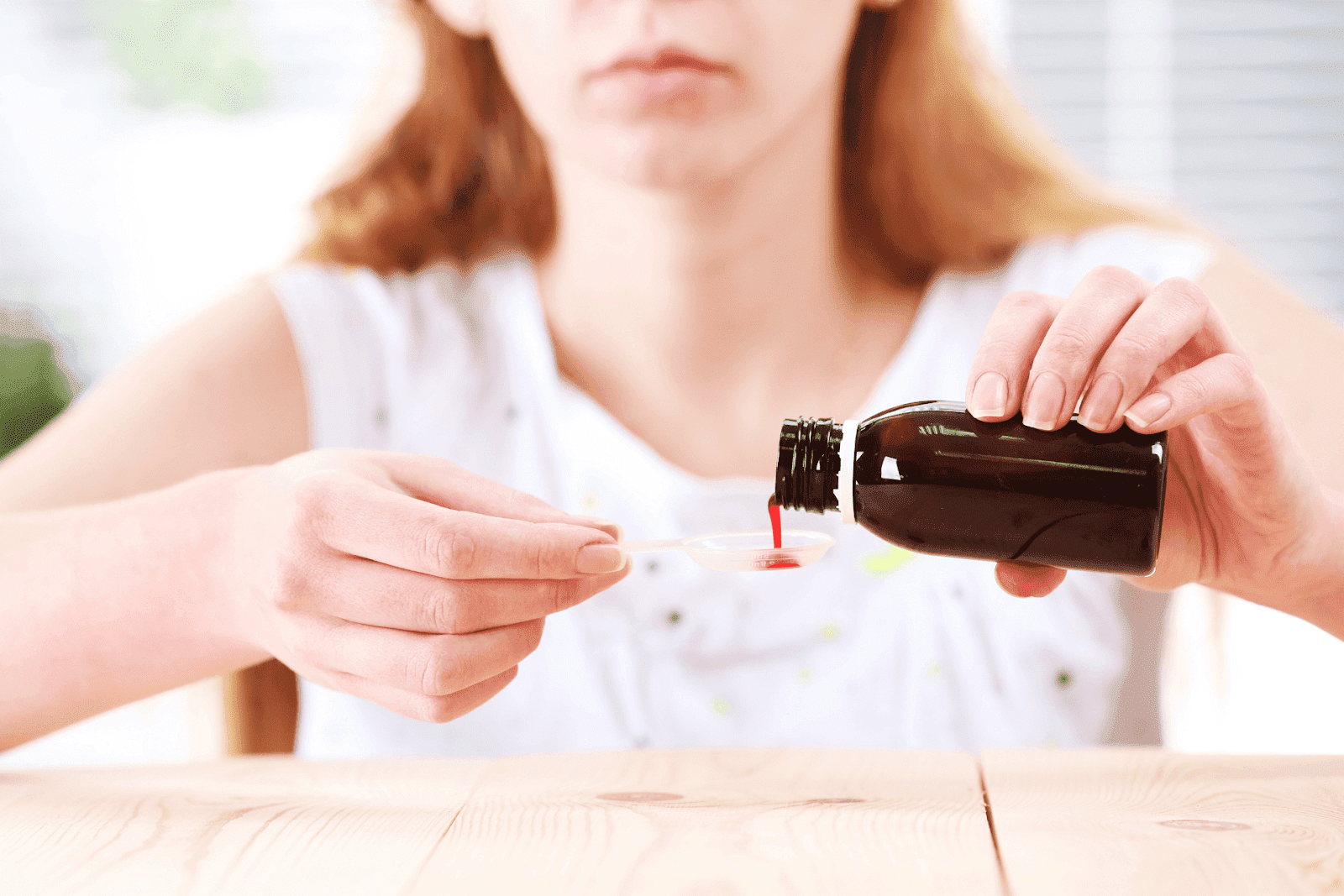 Woman pouring red liquid medicine from a brown bottle into a spoon.