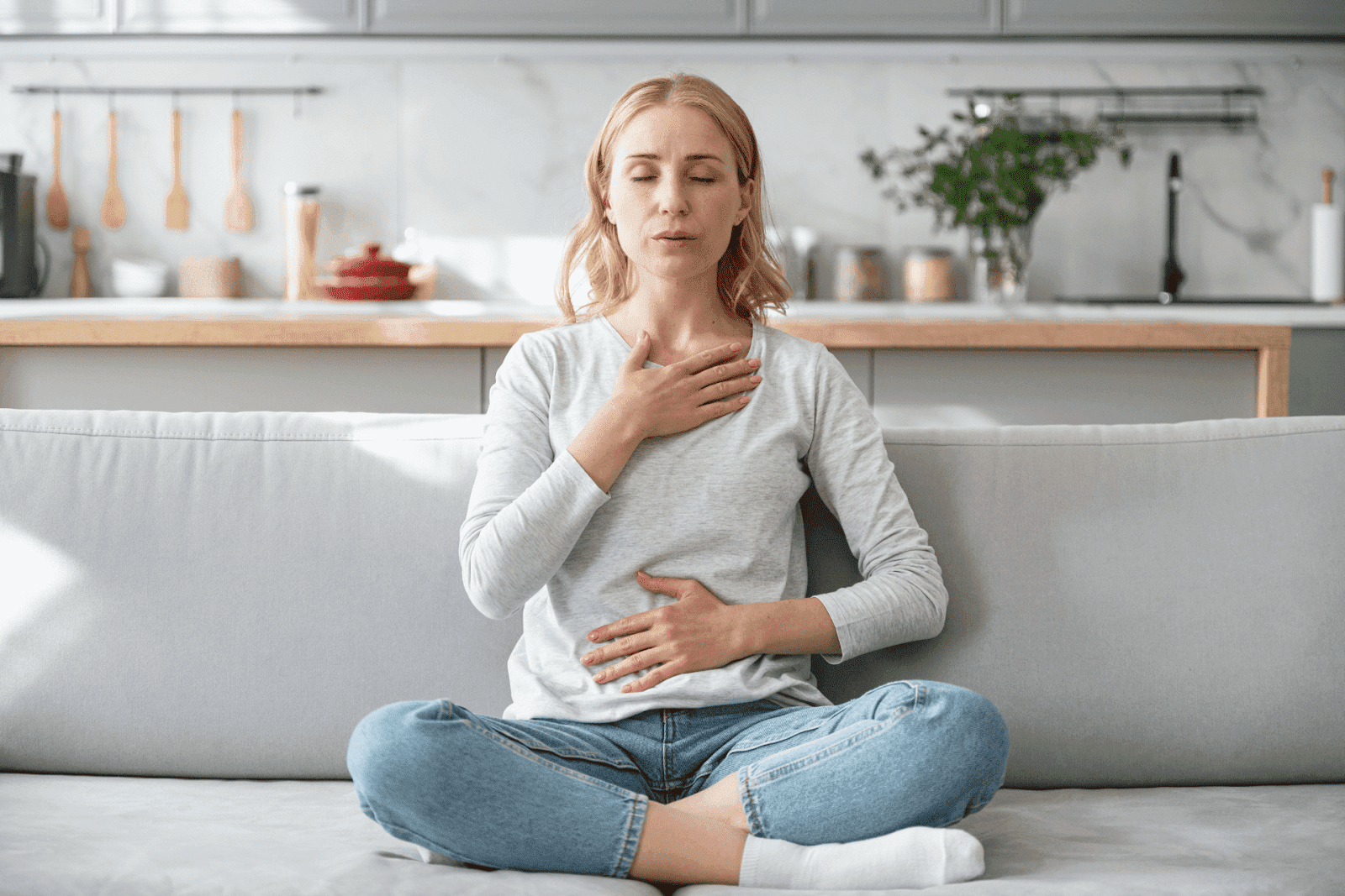 Woman practicing deep breathing exercise while sitting cross-legged on a couch.