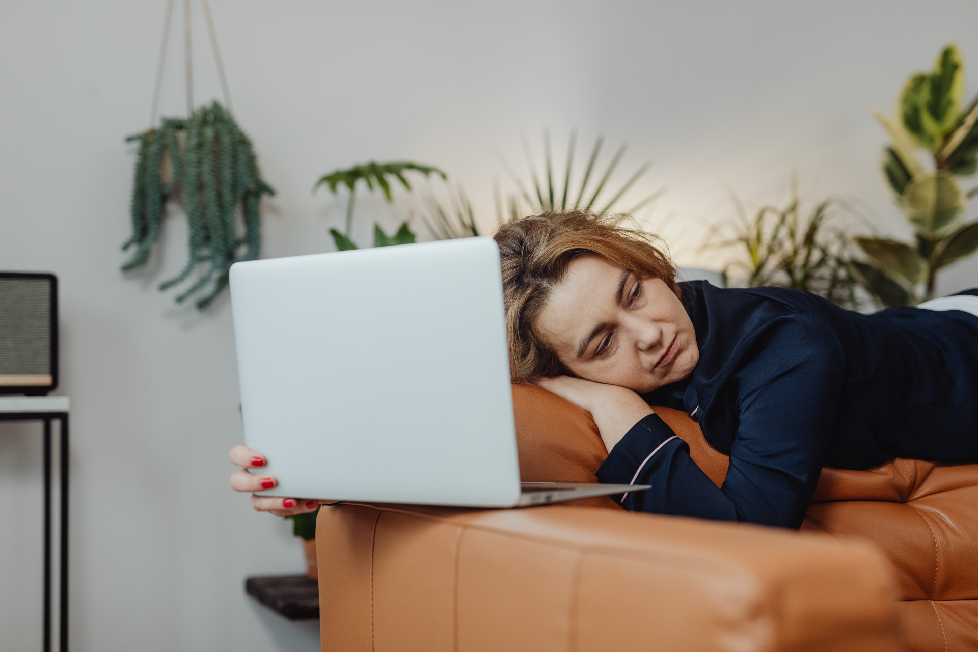 Woman resting her head on a couch while holding an open laptop, appearing tired or fatigued