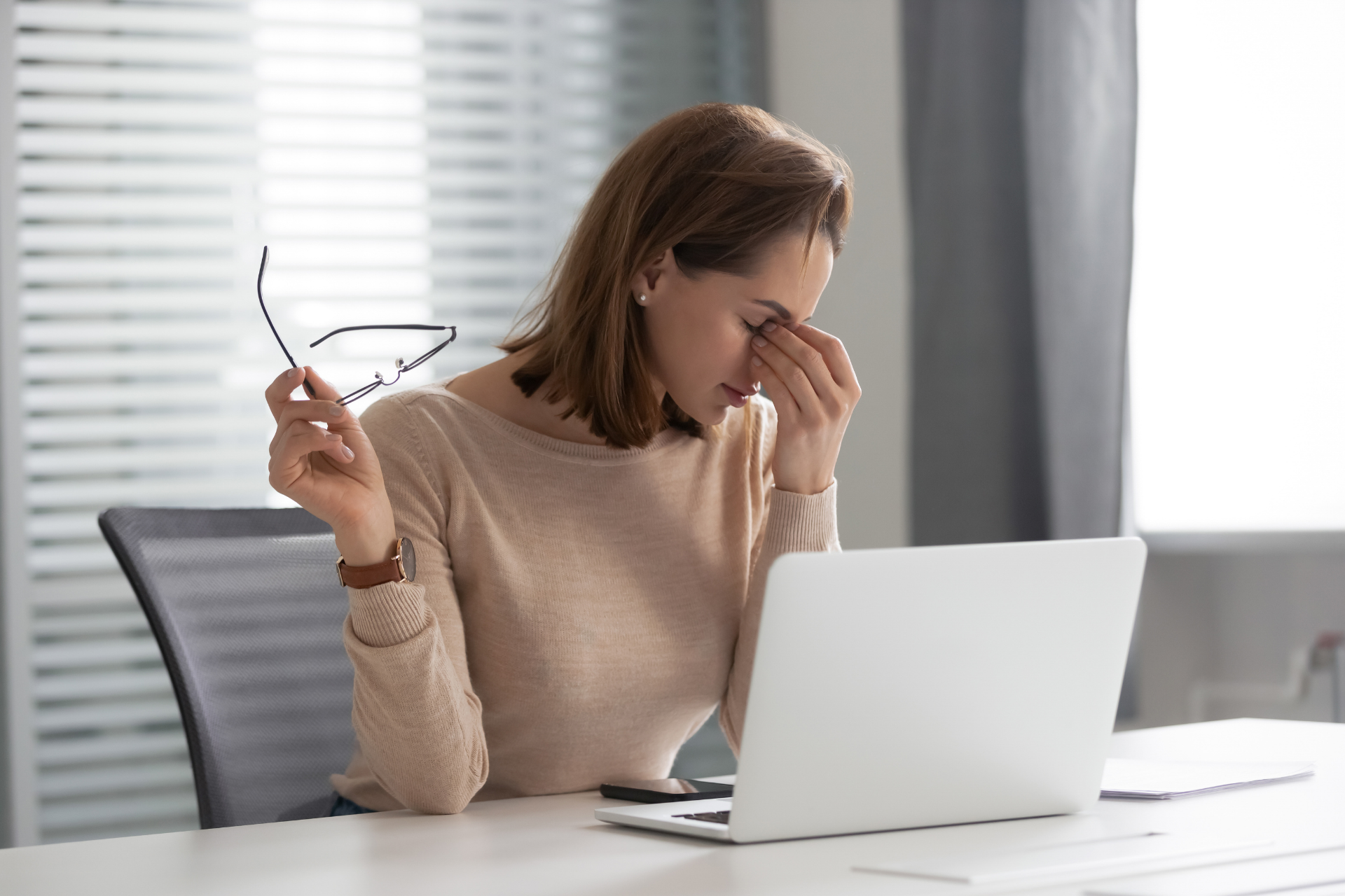 Woman rubbing her eyes while working on a laptop at a desk