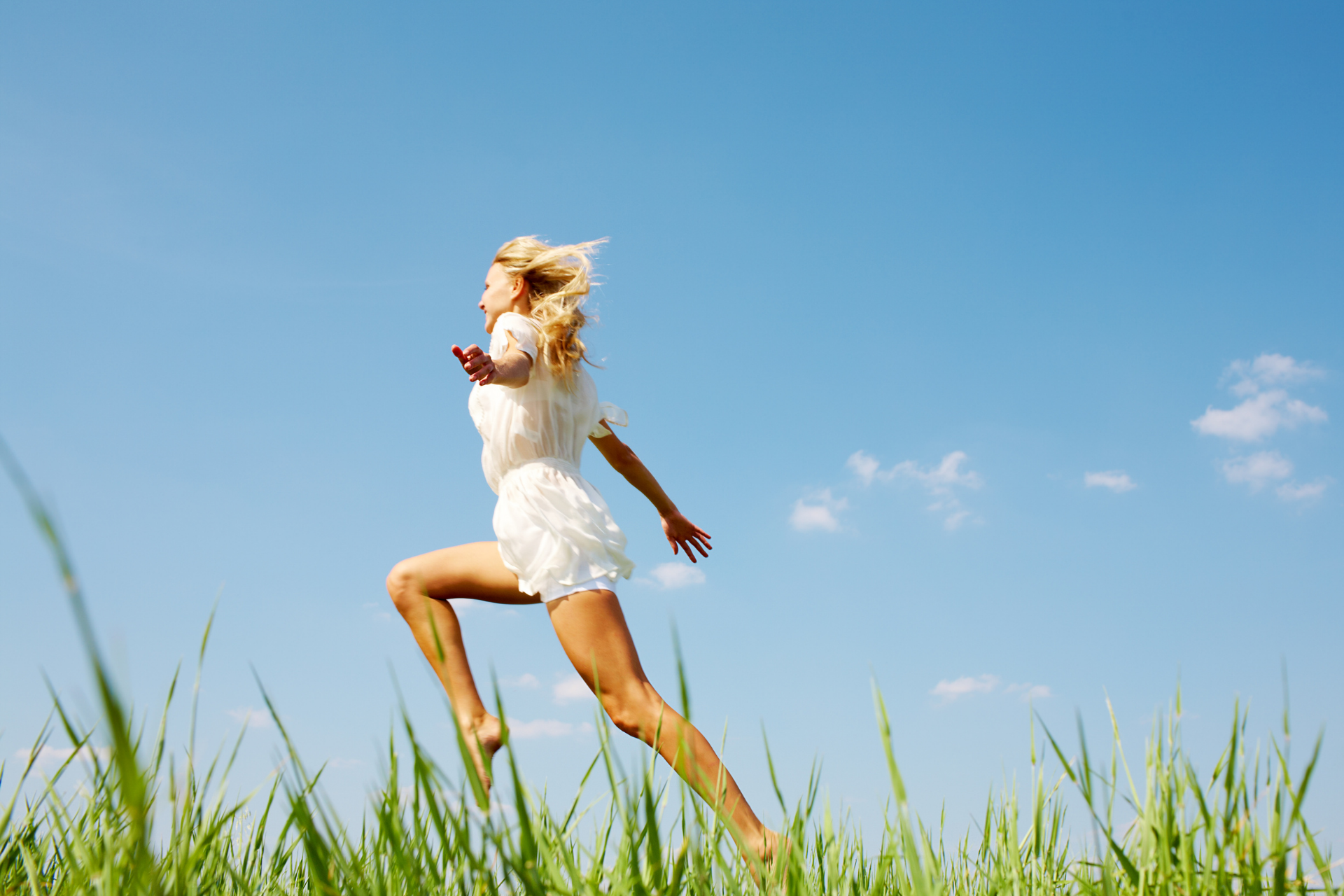 Woman running barefoot through grass under a clear blue sky