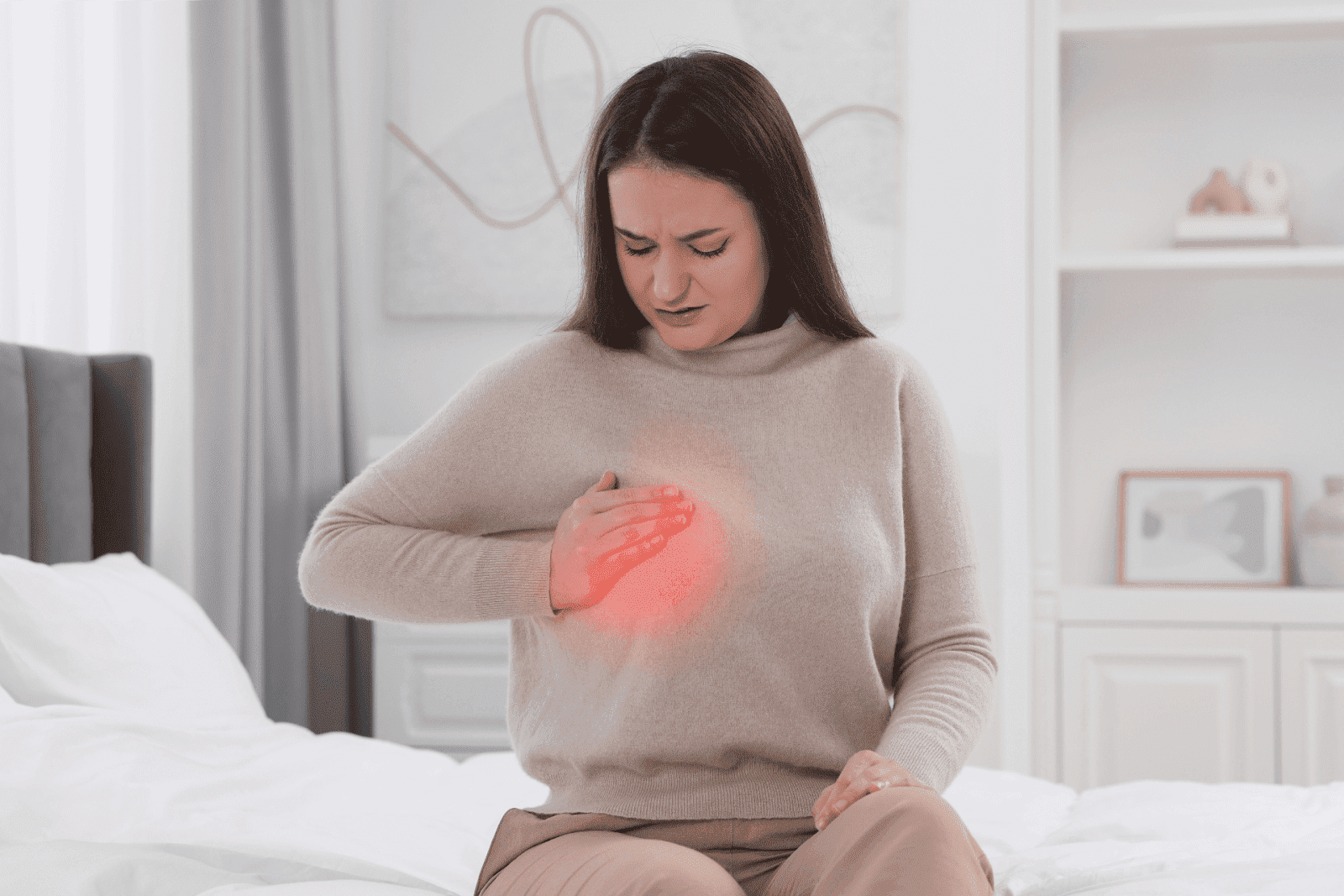 Woman sitting on a bed holding her chest with a red-highlighted pain area