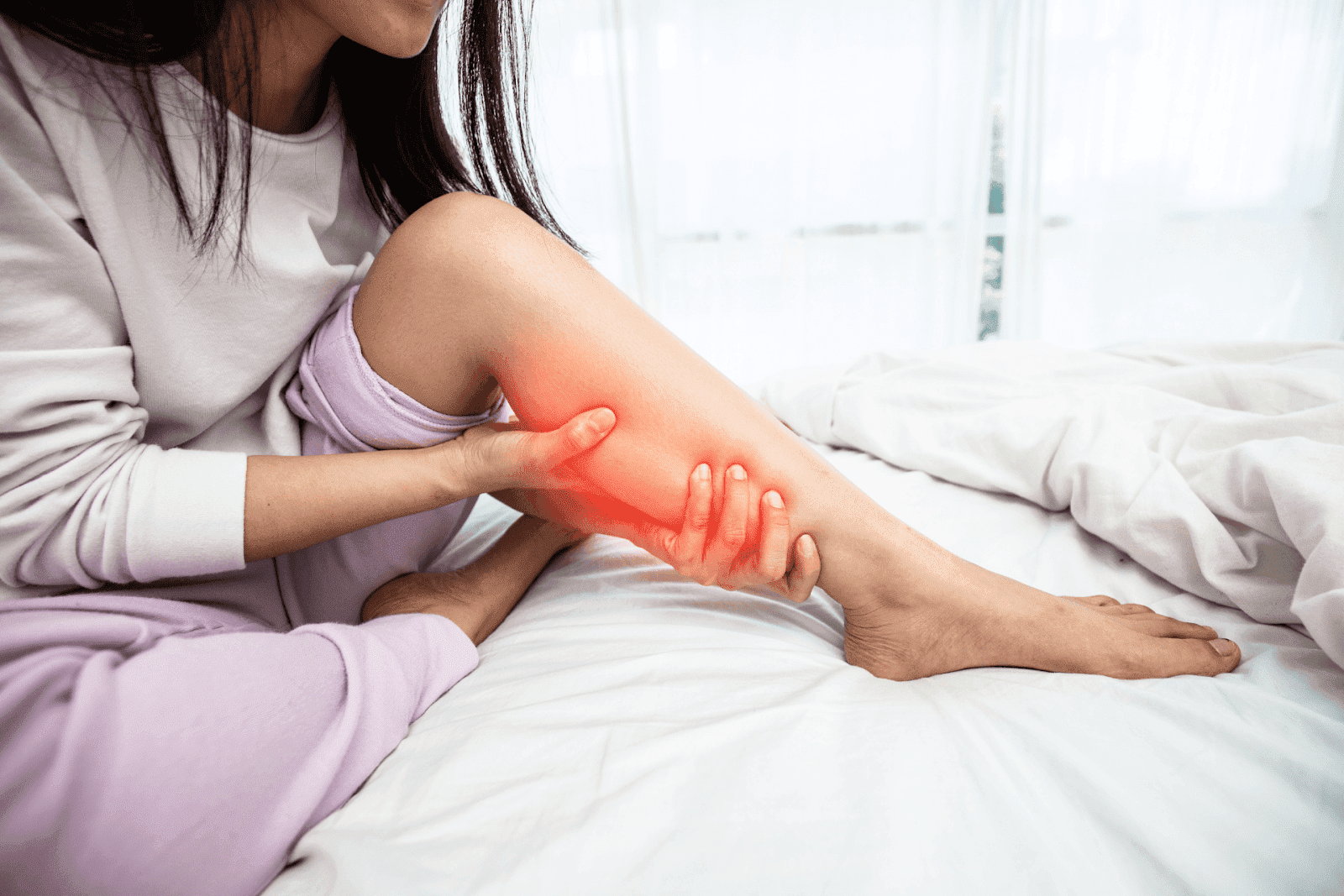 Woman sitting on a bed holding her leg with highlighted calf pain.