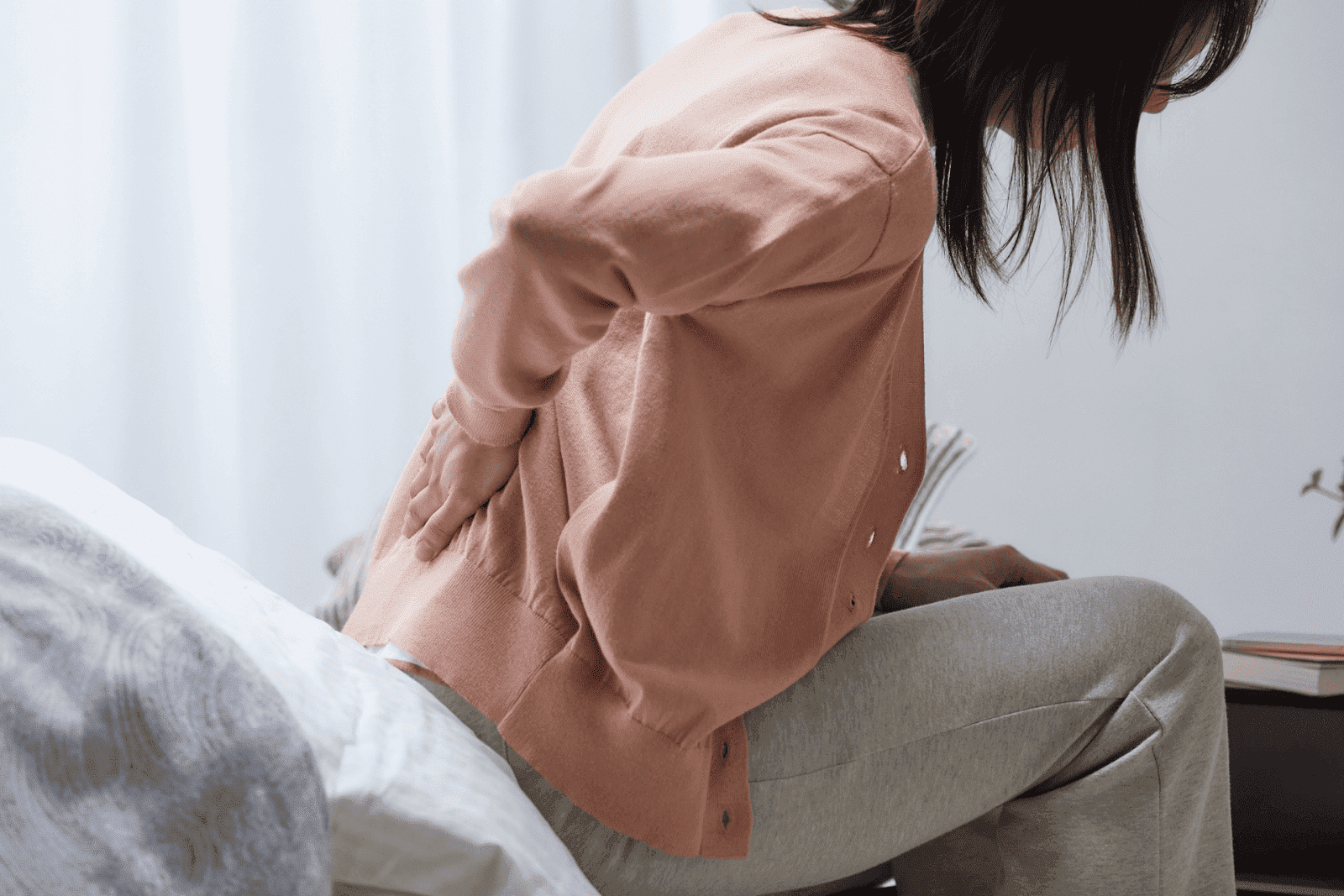 Woman sitting on a bed holding her lower back in pain.
