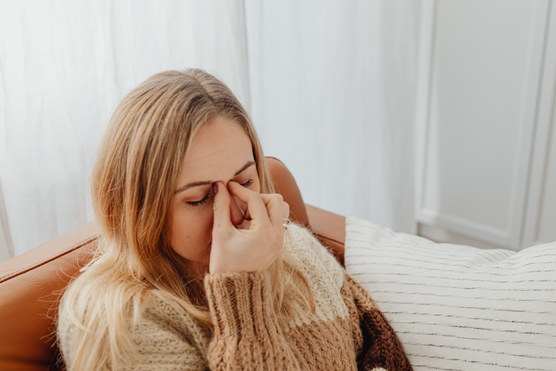 Woman sitting on a couch, pressing her fingers to her nose, appearing uncomfortable or congested