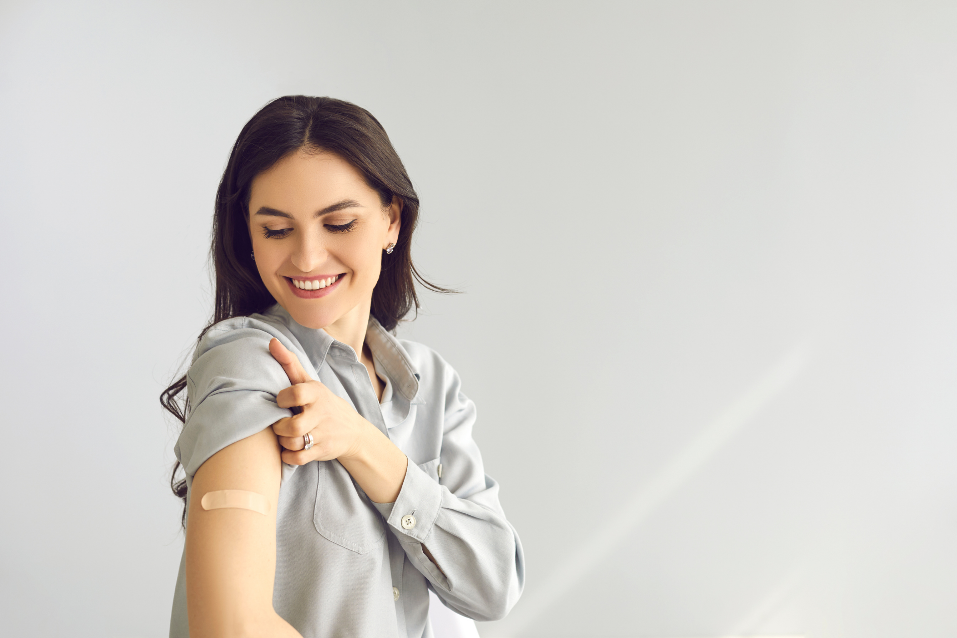 Woman smiling and looking at a bandage on her upper arm after a vaccination
