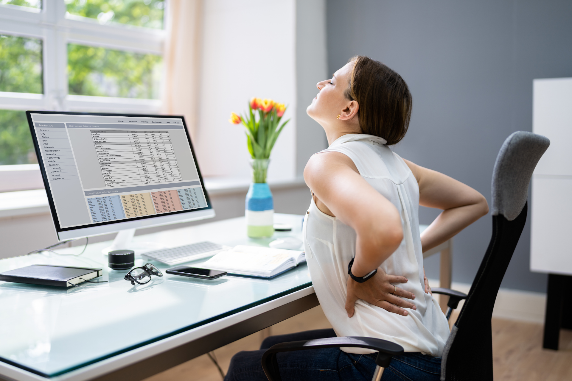 Woman stretching and holding her lower back in discomfort while sitting at a desk