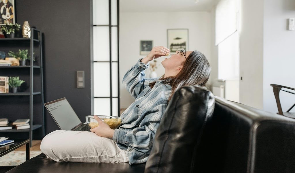 Woman sitting with laptop, trying to eat.
