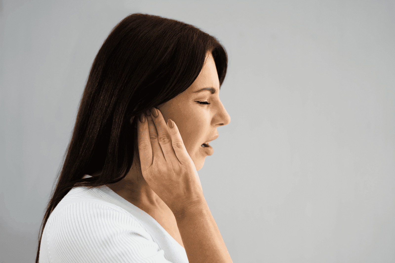 Woman touching her ear with a painful expression.