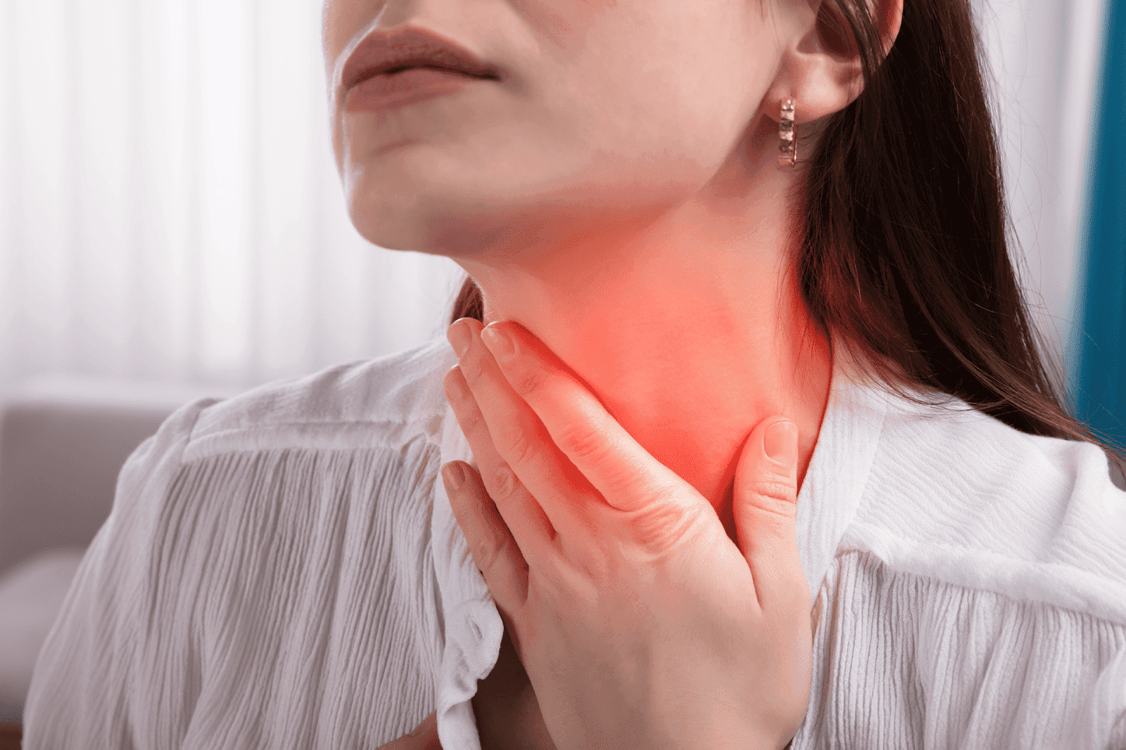 Woman touching her throat in discomfort, indicating pain or a sore throat.