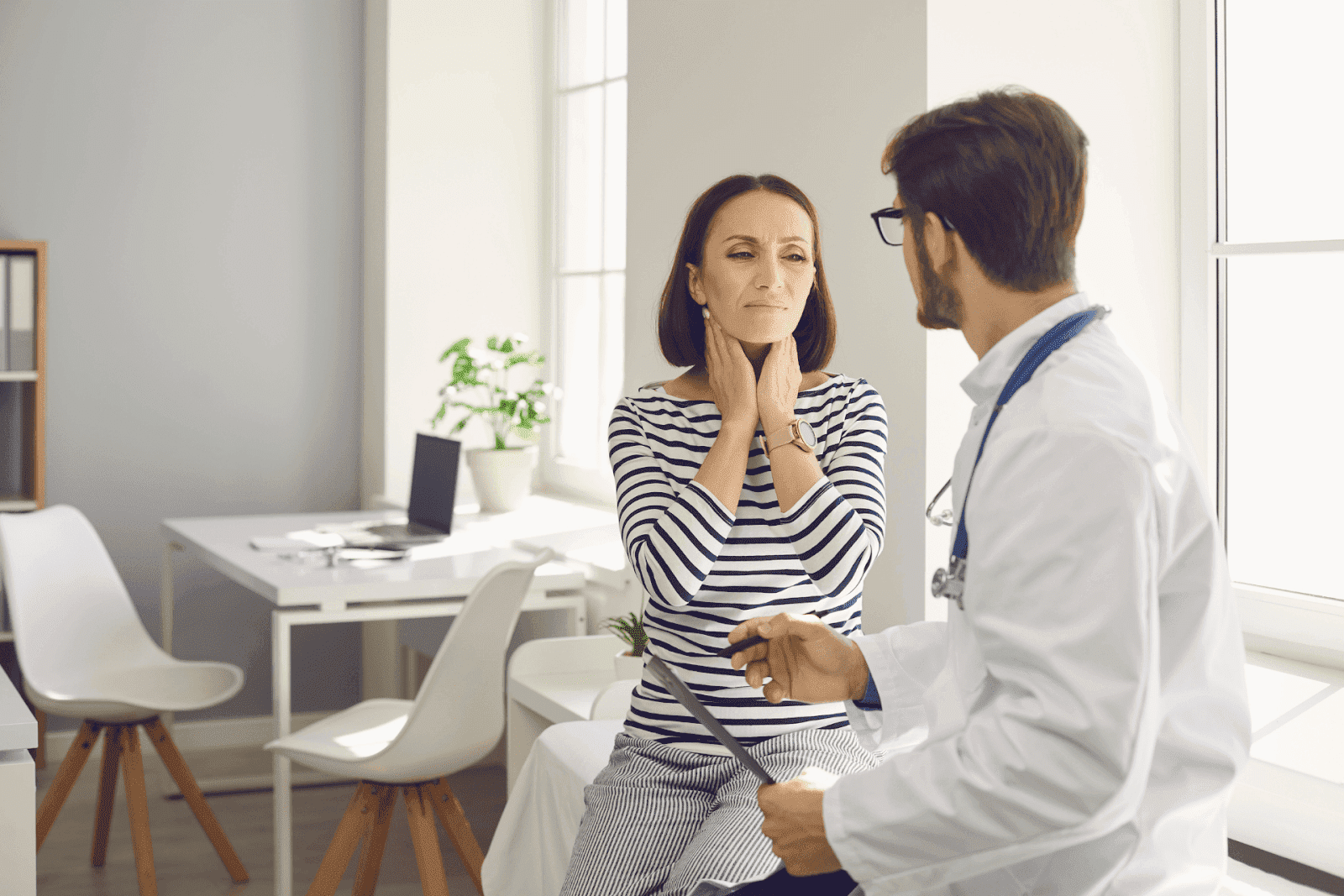 Woman touching neck while talking to doctor.