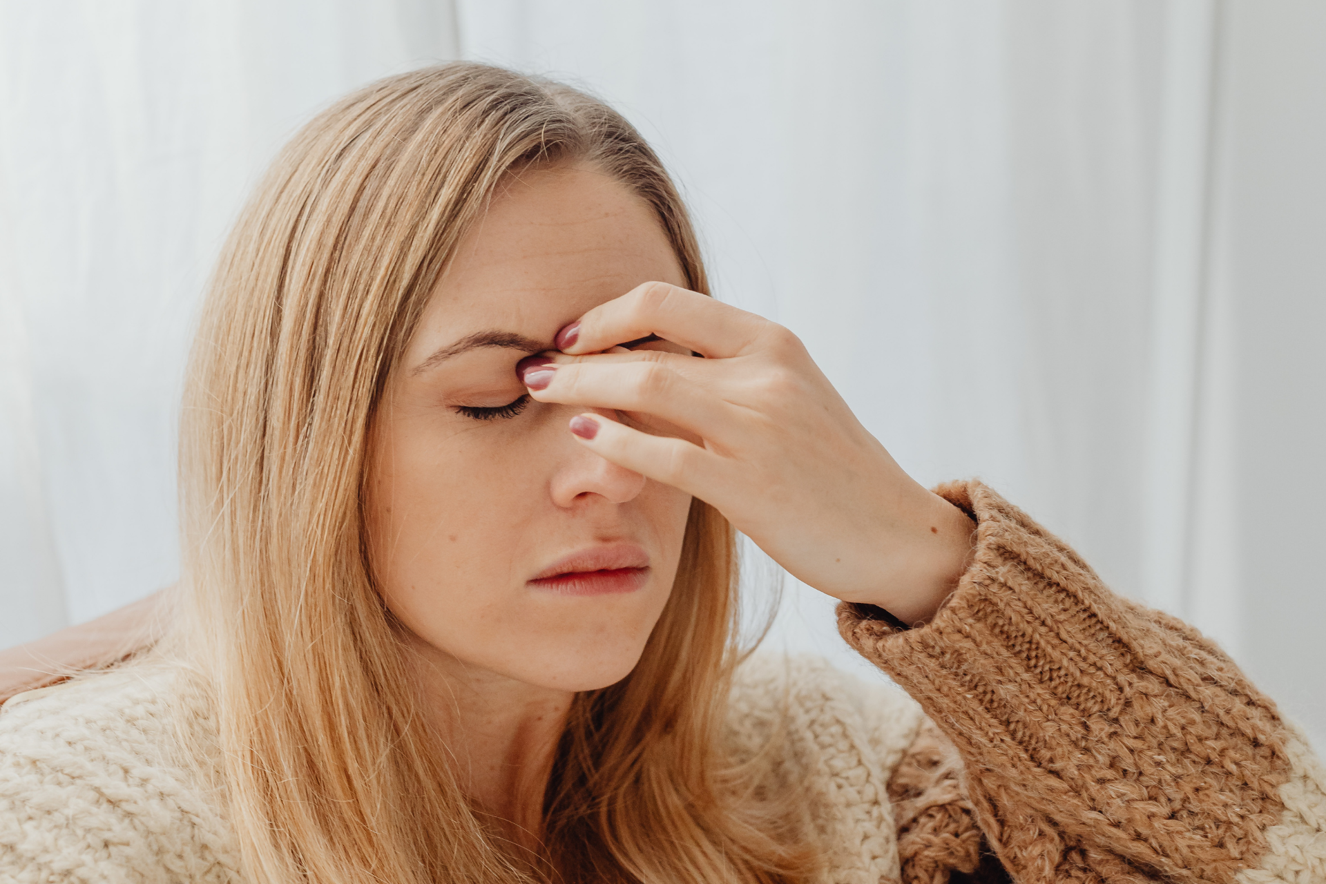 Woman with eyes closed, pressing fingers to her forehead, appearing fatigued or experiencing a headache