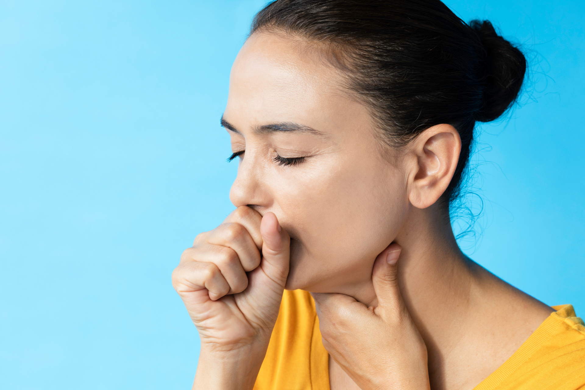 Woman with eyes closed, coughing into her fist against a blue background