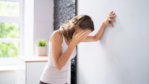 Woman with hand on right side of head and other hand on wall supporting herself up.